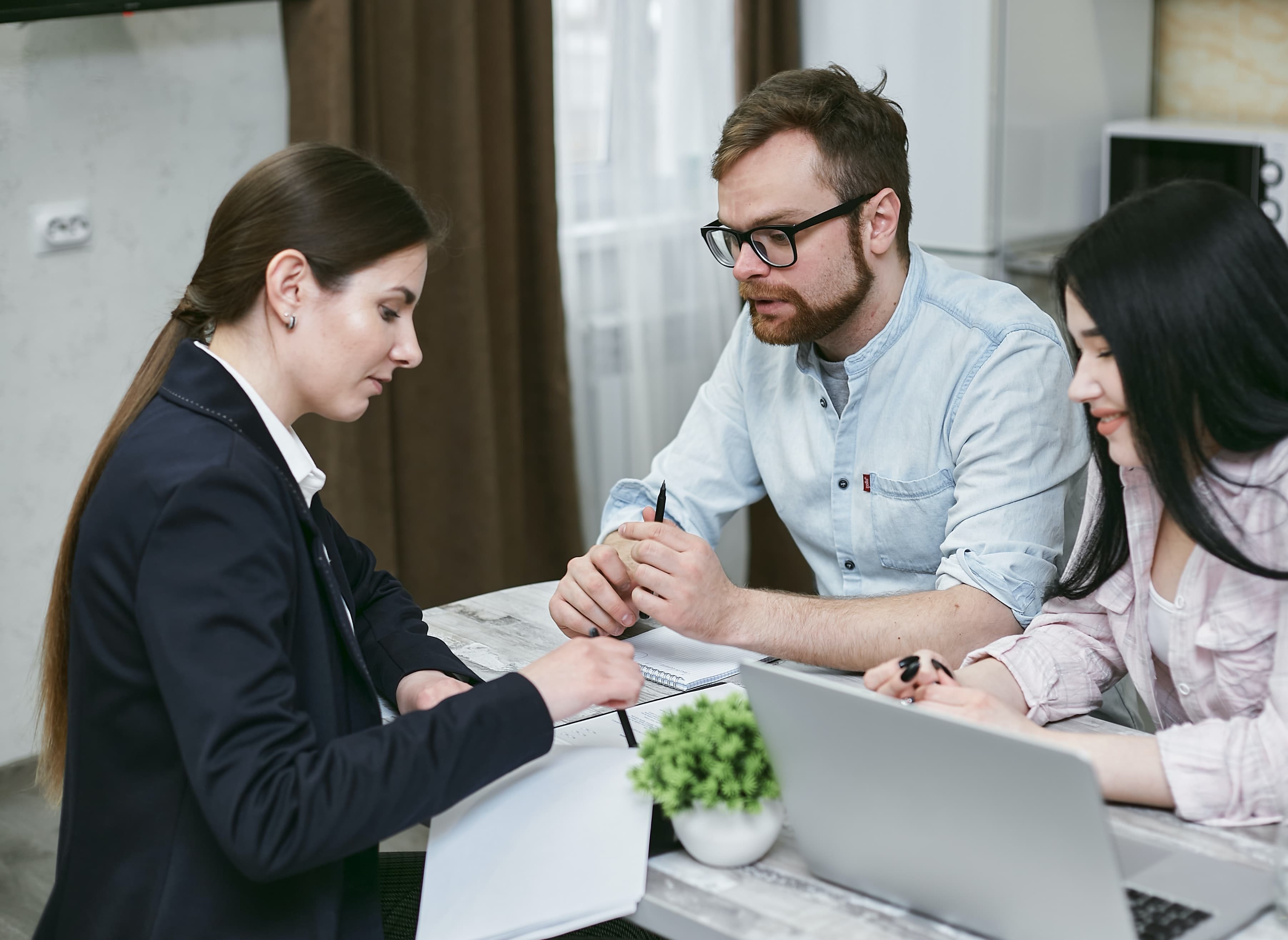 A couple sitting with a private lender, completing paperwork for a financial transaction.